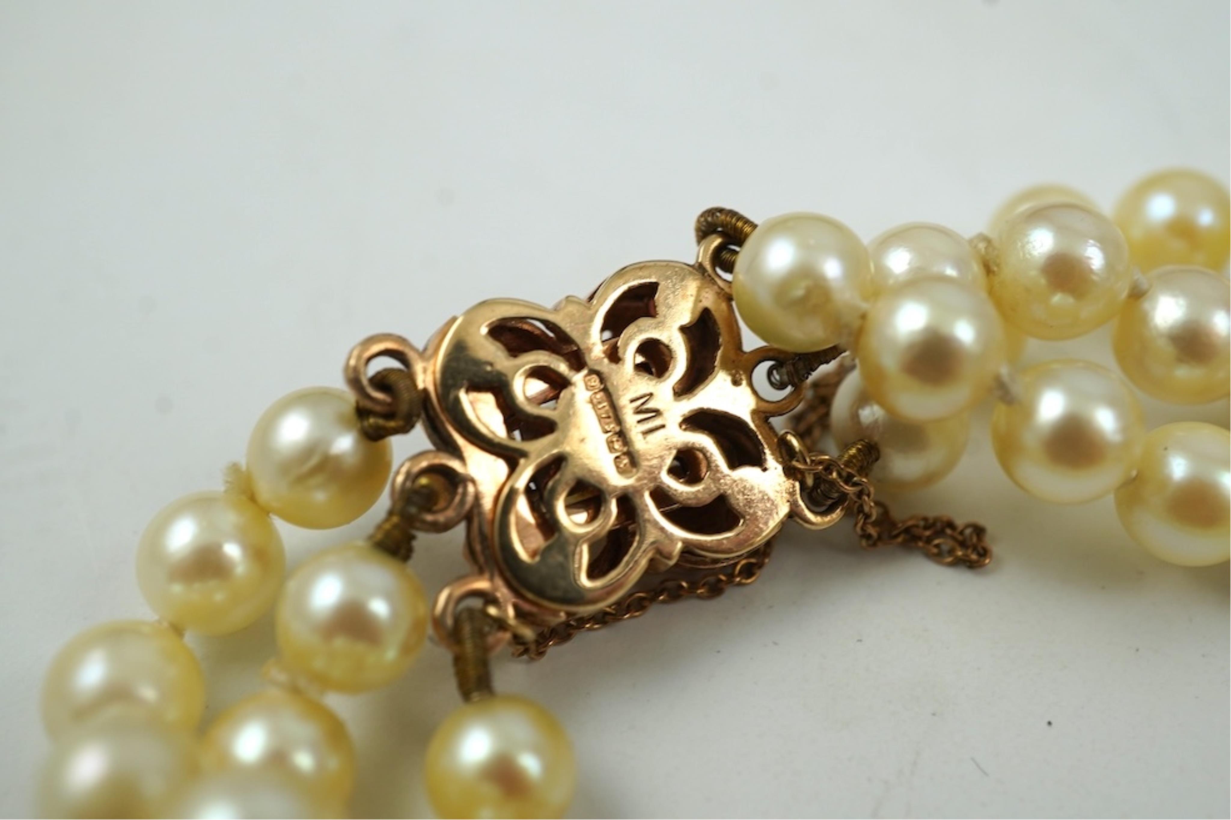 A triple strand cultured pearl bracelet, with a 9ct gold, garnet and cultured pearl cluster set clasp, 16cm.